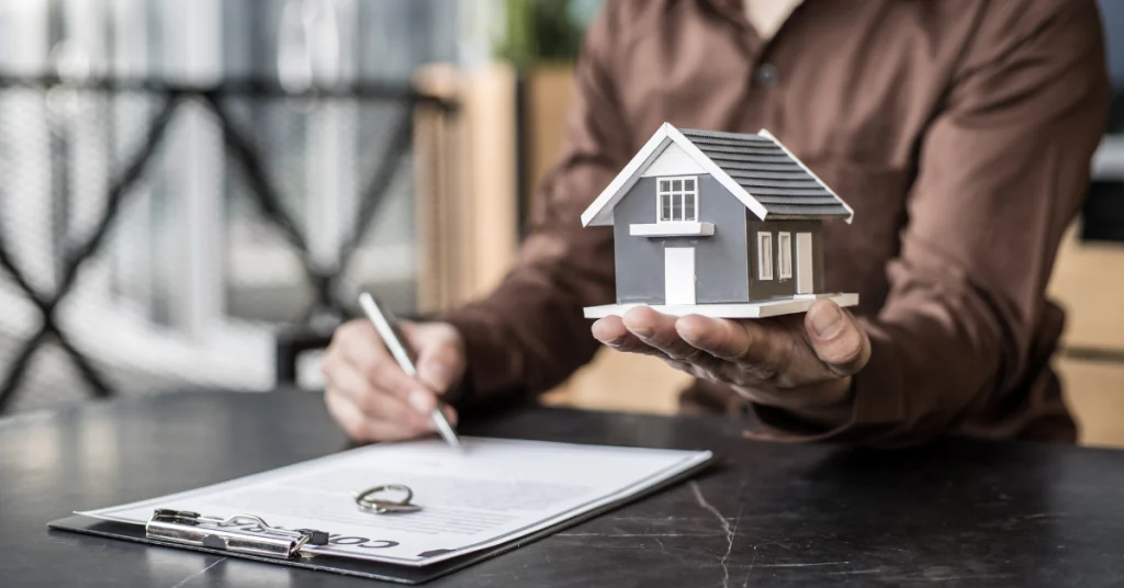 Corretor segura maquete de casa enquanto o comprador assina a transferência de propriedade